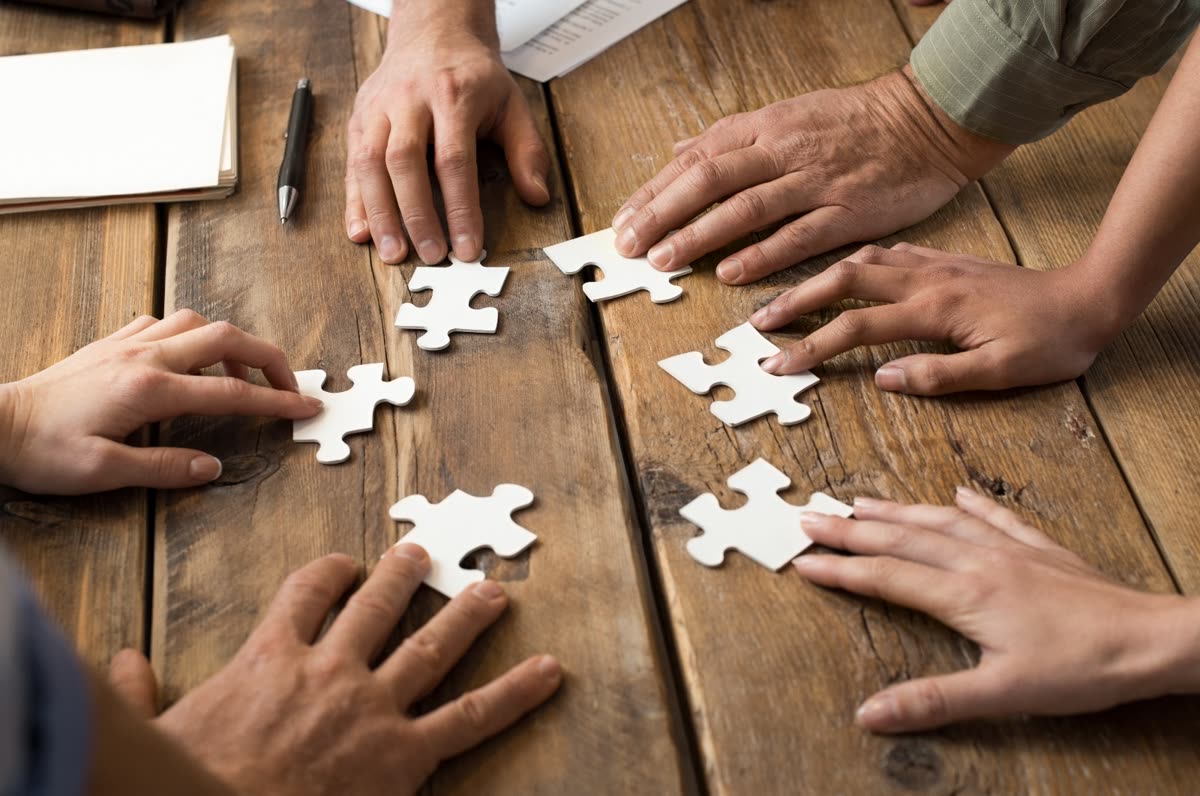 Hände legen gemeinsam ein Puzzle zusammen